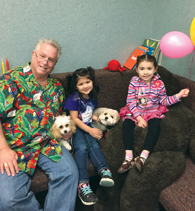 Lexa and Flossie: (From left) Dr. Alan Golden, Elysia Yriarte and Natalia Caraballo smile for the camera while petting Flossie, a dental therapy dog, and her half-sister Lexa, a dental therapy dog-in-training. (photo courtesy of American Dental Association)